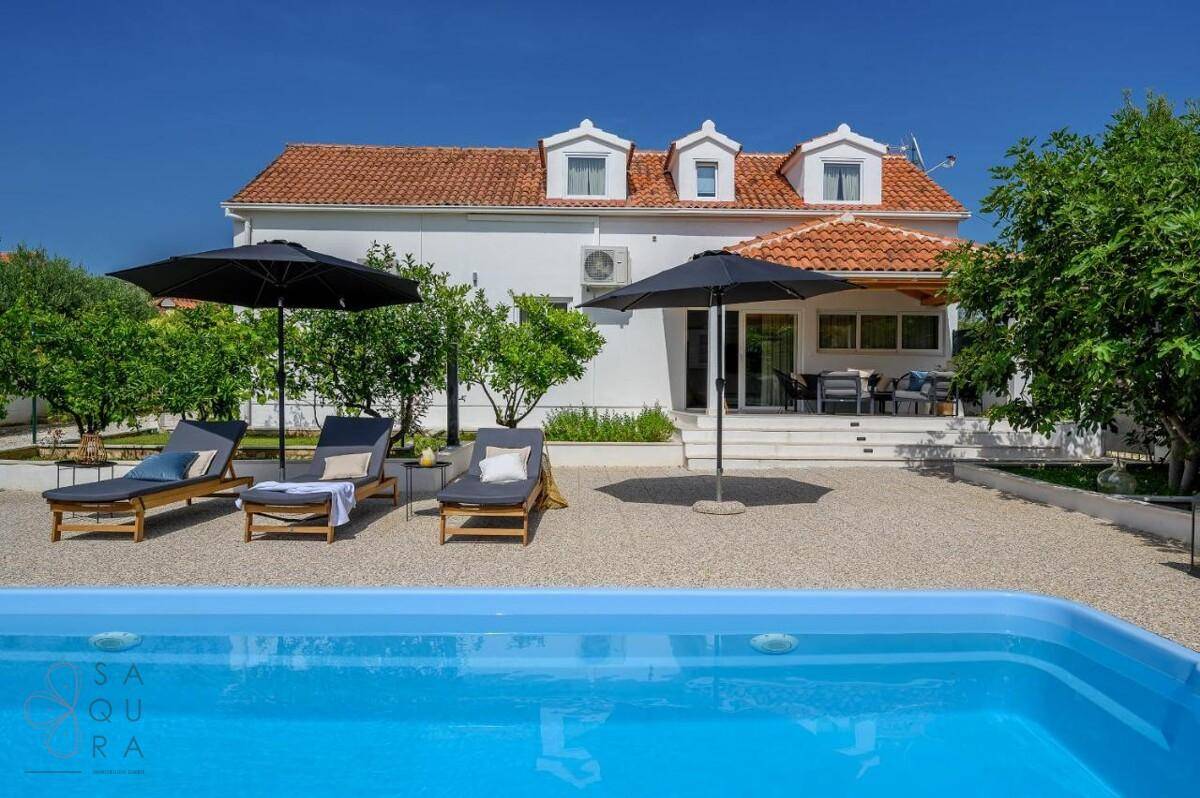Sonniger Poolbereich mit Liegestühlen und Sonnenschirmen vor dem charmanten Haus.