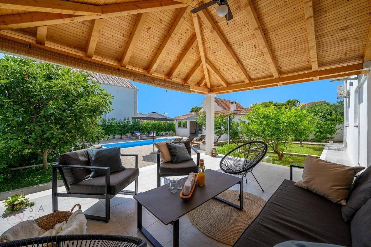 Sonnige überdachte Terrasse mit bequemen Sitzmöbeln und Blick auf den Poolbereich.