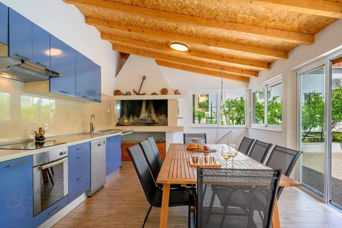 Helle Küche mit blauen Schränken, Essbereich und großem Grillkamin unter Holzdach.