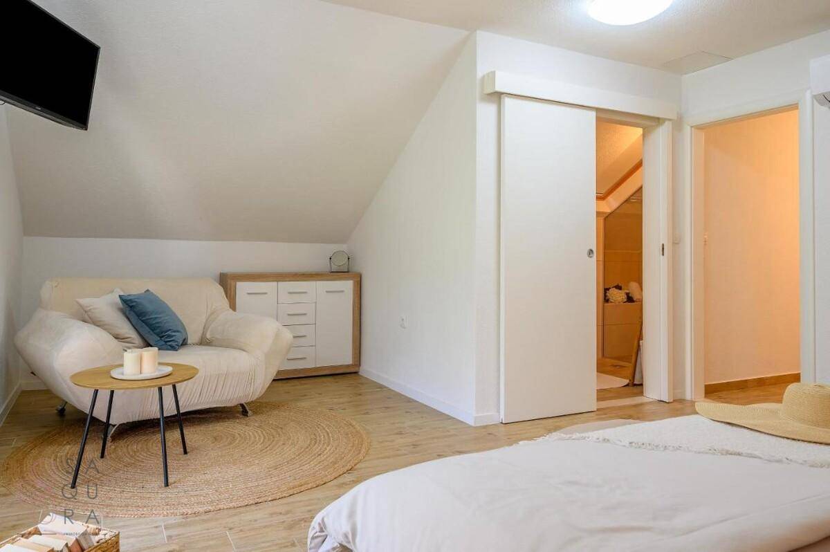 Helles Schlafzimmer im Dachgeschoss mit Doppelbett, Sofa und Schiebetür zum Bad.