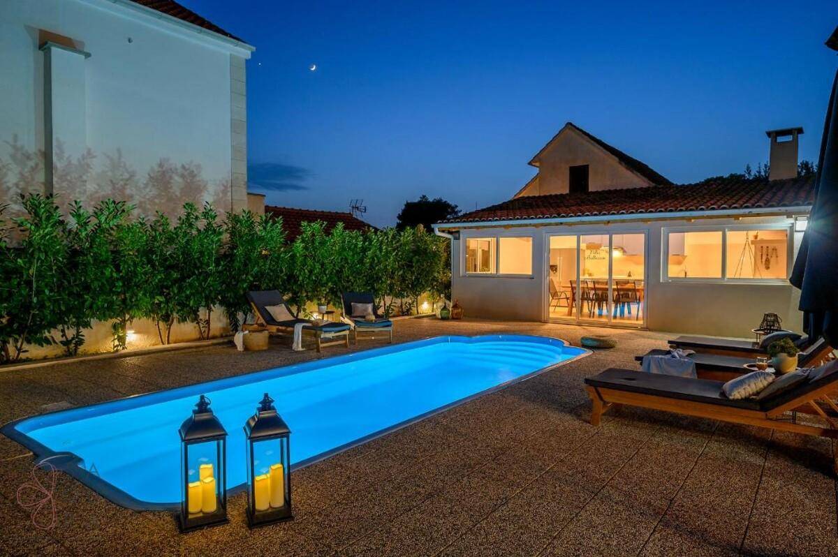 Ruhiger Poolbereich mit Liegestühlen und Laternen, umgeben von Gebäuden in der Abenddämmerung.