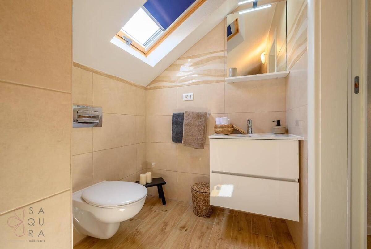 Kleines Badezimmer im Dachgeschoss mit Toilette, Waschtisch und Dachfenster.