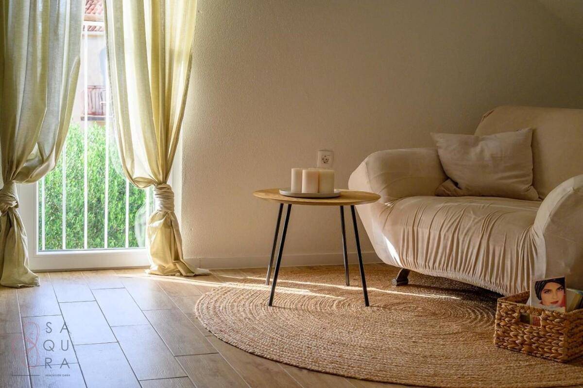 Helles Wohnzimmer mit beigem Sessel, Holzboden und französischem Balkon.
