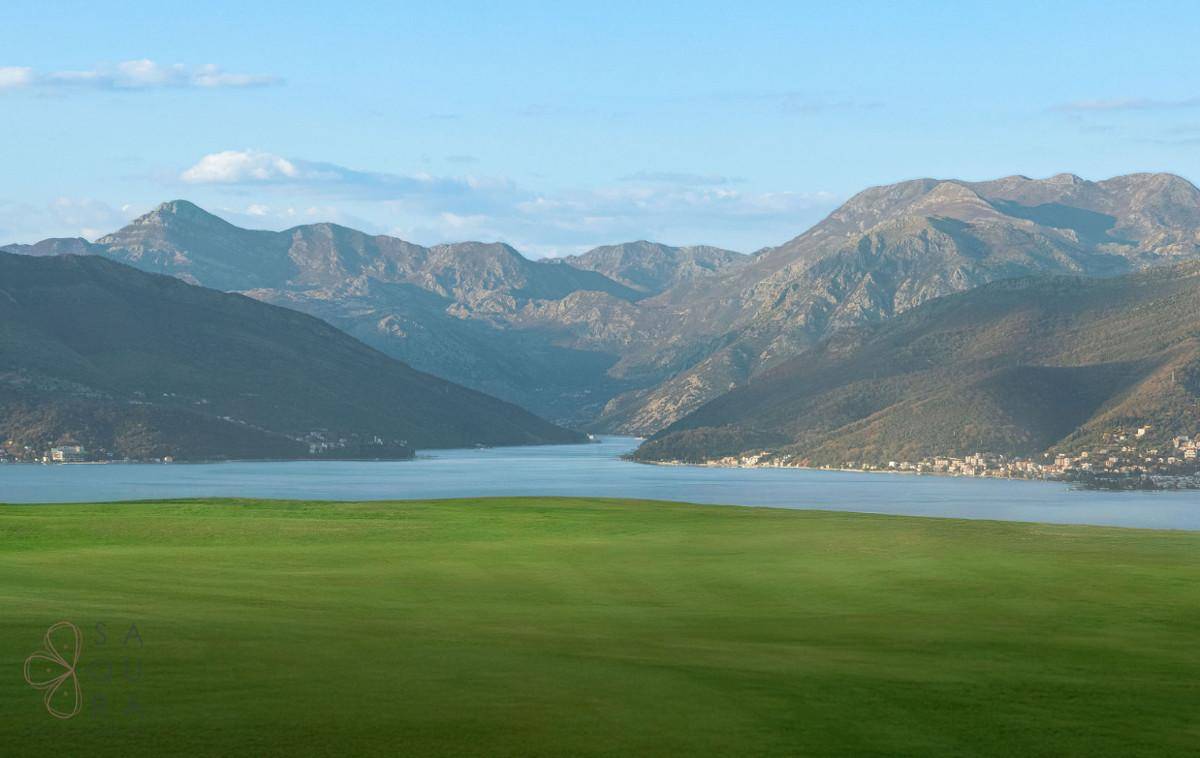Weitläufiger Panoramablick auf eine ruhige Bucht, umgeben von majestätischen Bergen unter blauem Himmel.