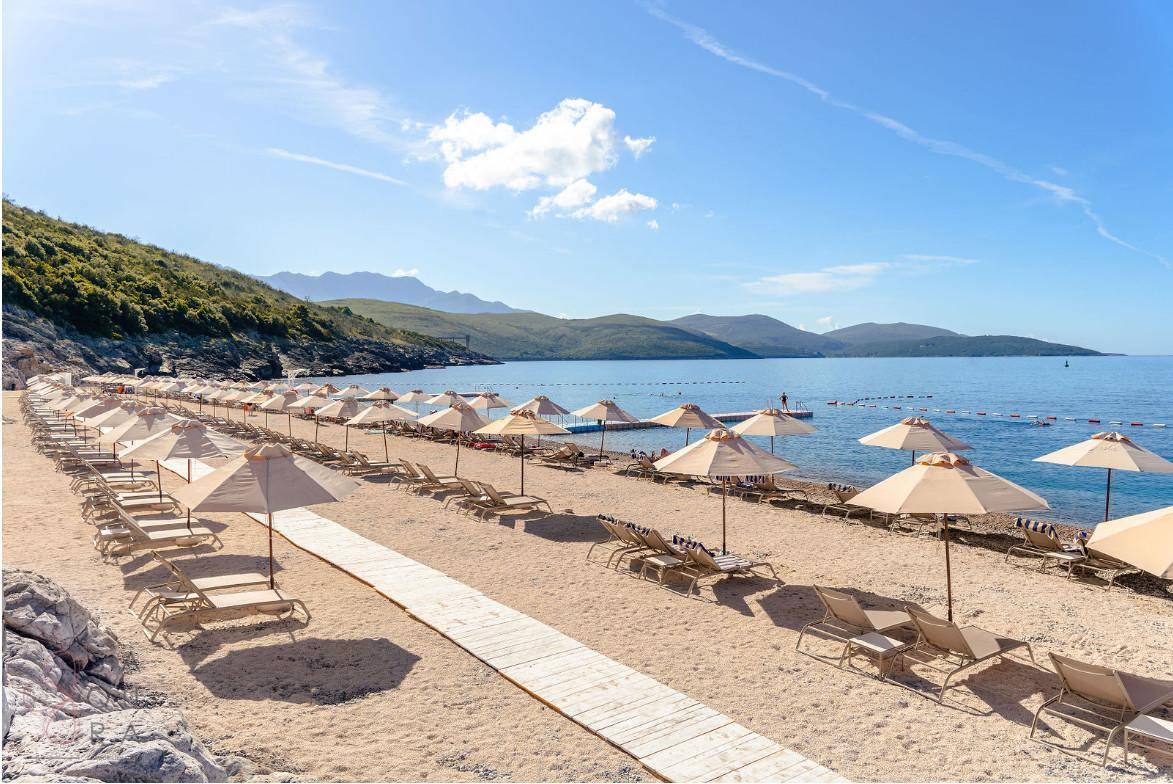 Sandstrand mit Reihen von Sonnenliegen und Sonnenschirmen unter blauem Himmel.