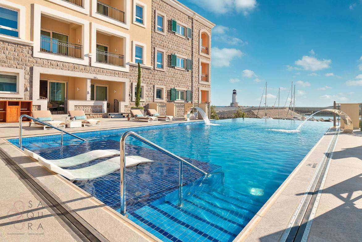 Moderner Außenpool mit blauen Fliesen und Wasserspielen, angrenzend an ein Gebäude mit Blick auf den Yachthafen.