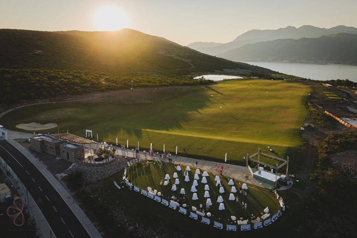Weitläufige Grünfläche, möglicherweise ein Golfplatz, mit einer Event-Location bei Sonnenuntergang.