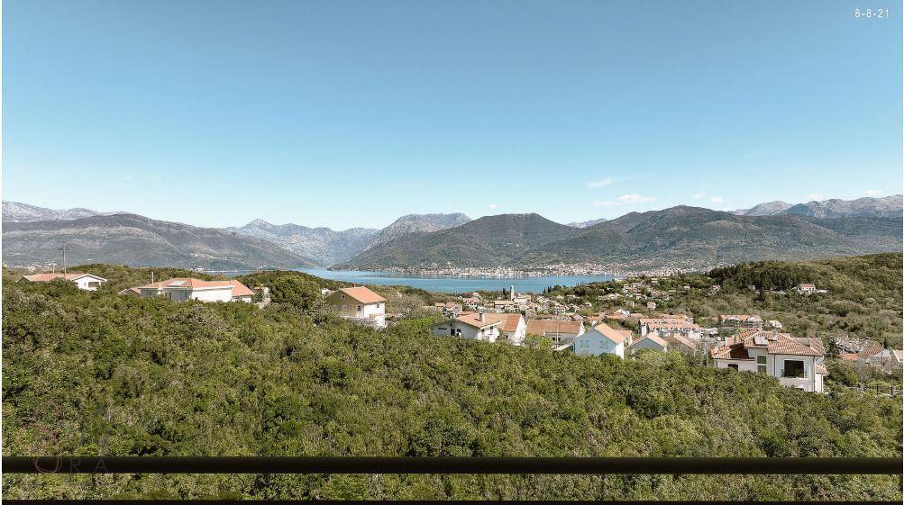 Weitläufiger Blick über grüne Hügel auf das Meer und die majestätischen Berge in der Ferne.