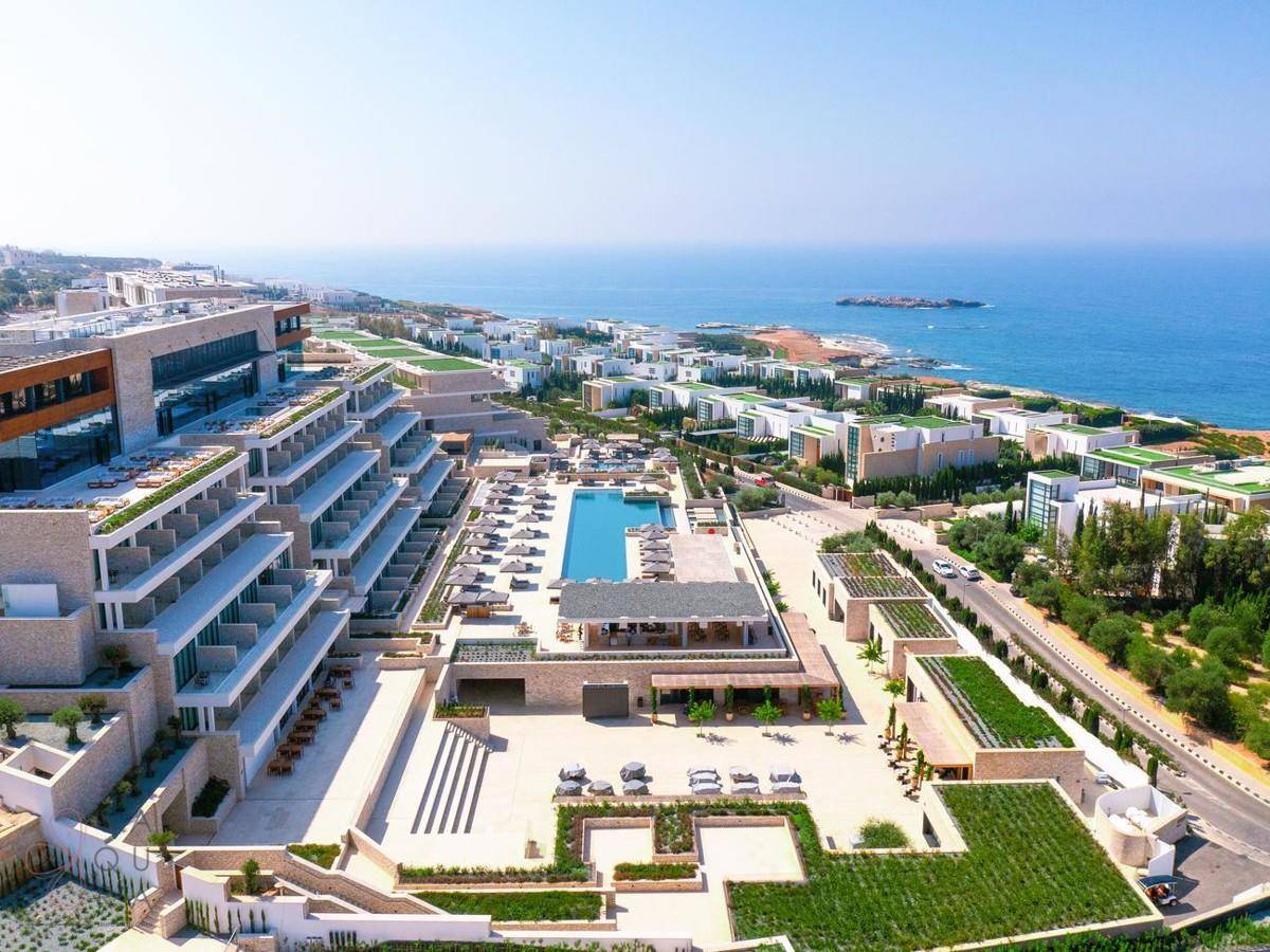 Große Hotelanlage mit weitläufigen Poolbereichen und Meerblick, umgeben von modernen Wohnhäusern.