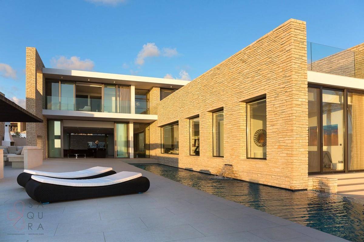 Elegante Villa mit privatem Pool, Sonnenliegen und moderner Steinverkleidung unter blauem Himmel.