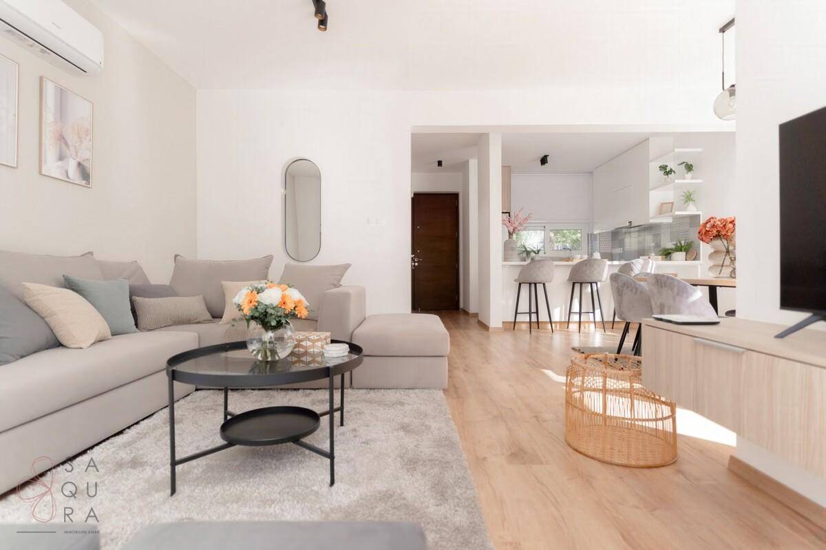 Offener Wohnbereich mit Holzboden, modernem Sofa und Blick auf die Küche.