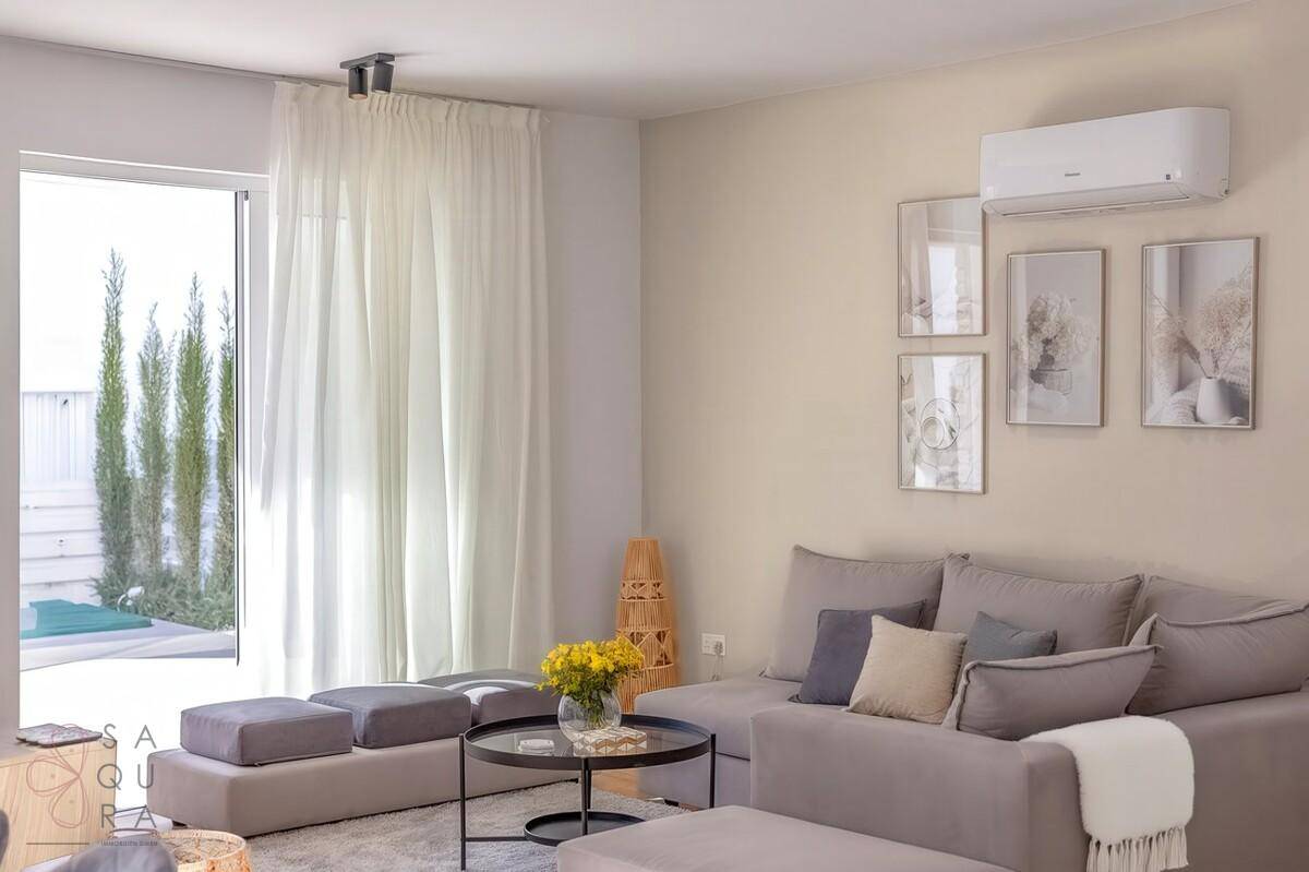 Gemütliches Wohnzimmer mit modernem Sofa, Klimaanlage und Blick auf den Außenbereich.