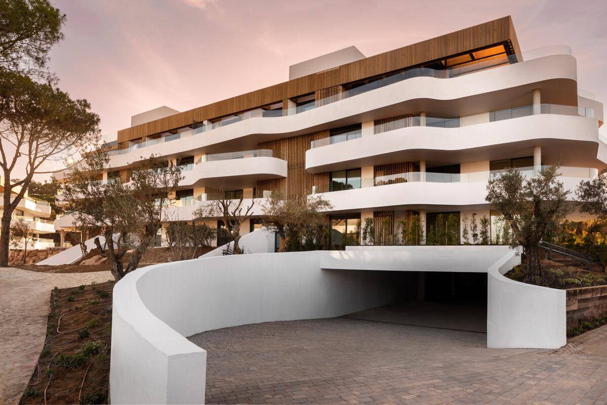 Modernes Apartmentgebäude bei Sonnenuntergang, mit geschwungener Architektur und Tiefgaragenzufahrt.