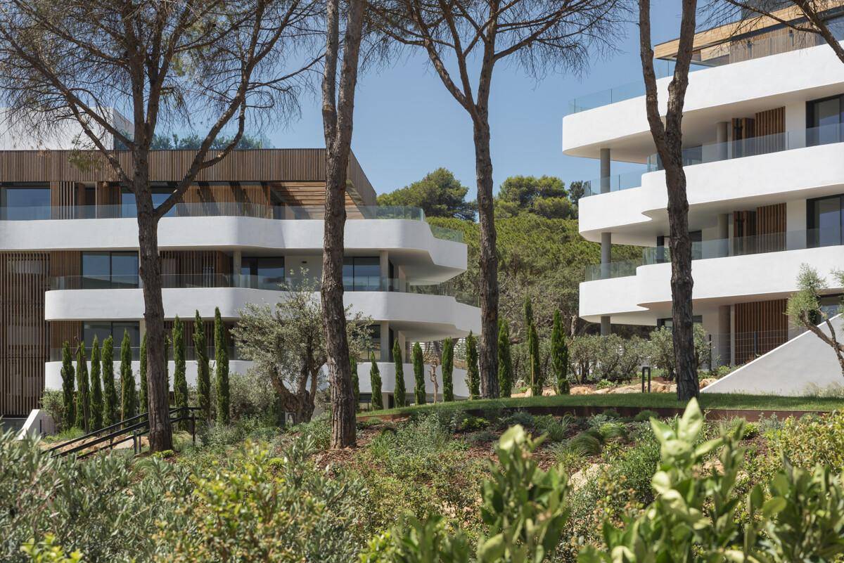 Moderne Wohngebäude mit geschwungenen Balkonen, eingebettet in eine grüne, mediterrane Landschaft.