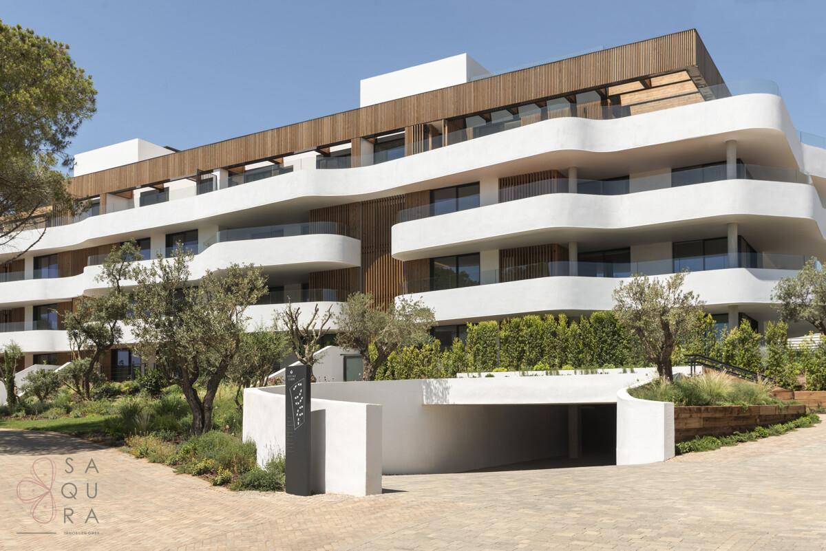 Elegante moderne Wohnanlage mit geschwungenen Balkonen, Holzfassade und Tiefgaragenzufahrt.