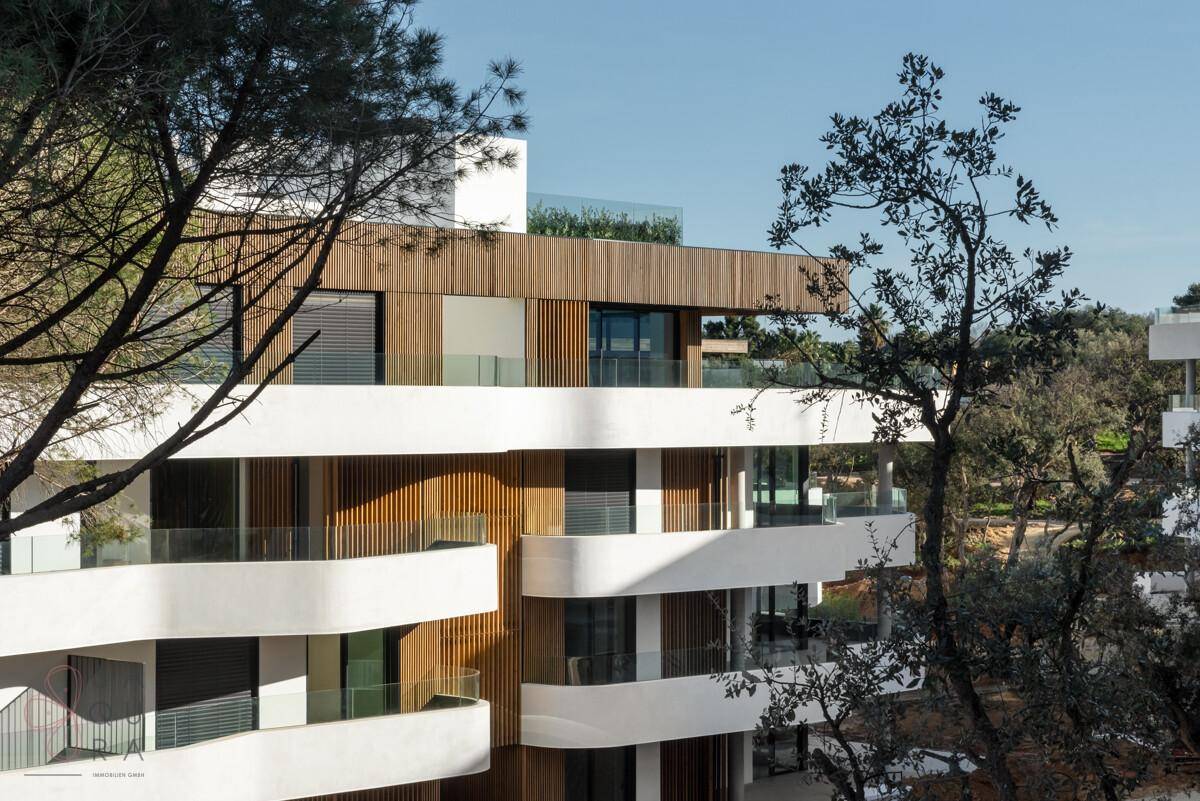 Moderne Wohnanlage mit geschwungenen Balkonen und Holzdetails, eingebettet in eine grüne Landschaft.