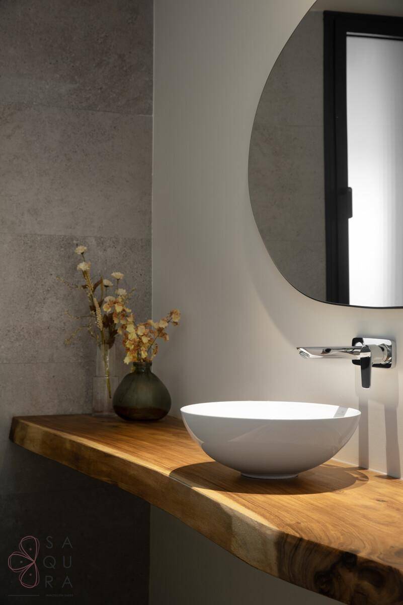 Modernes Badezimmer mit stilvollem Waschbecken auf einer Holzplatte und rundem Spiegel.
