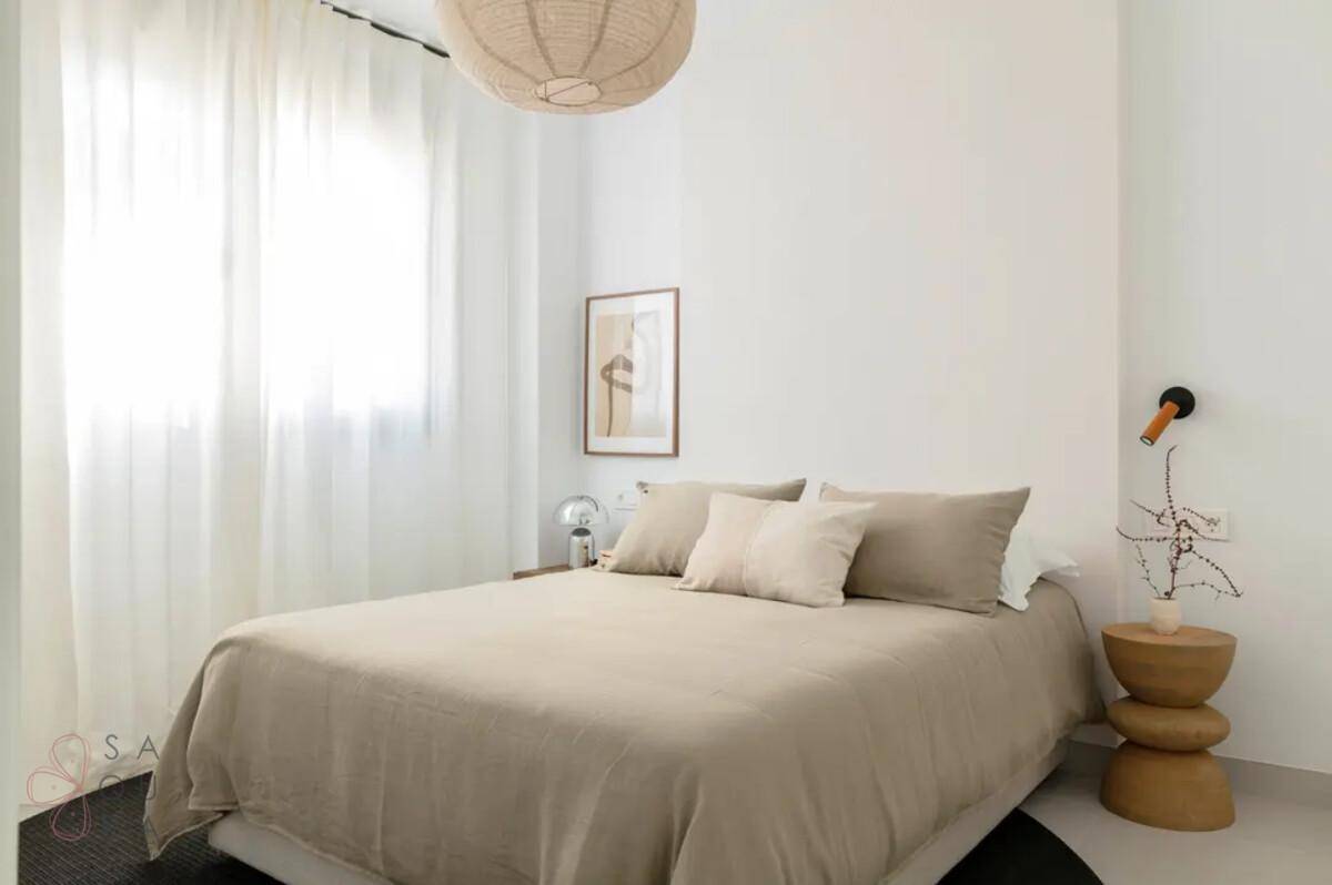 Gemütliches Schlafzimmer mit Doppelbett, beiger Bettwäsche und einem großen Fenster für natürliche Beleuchtung.