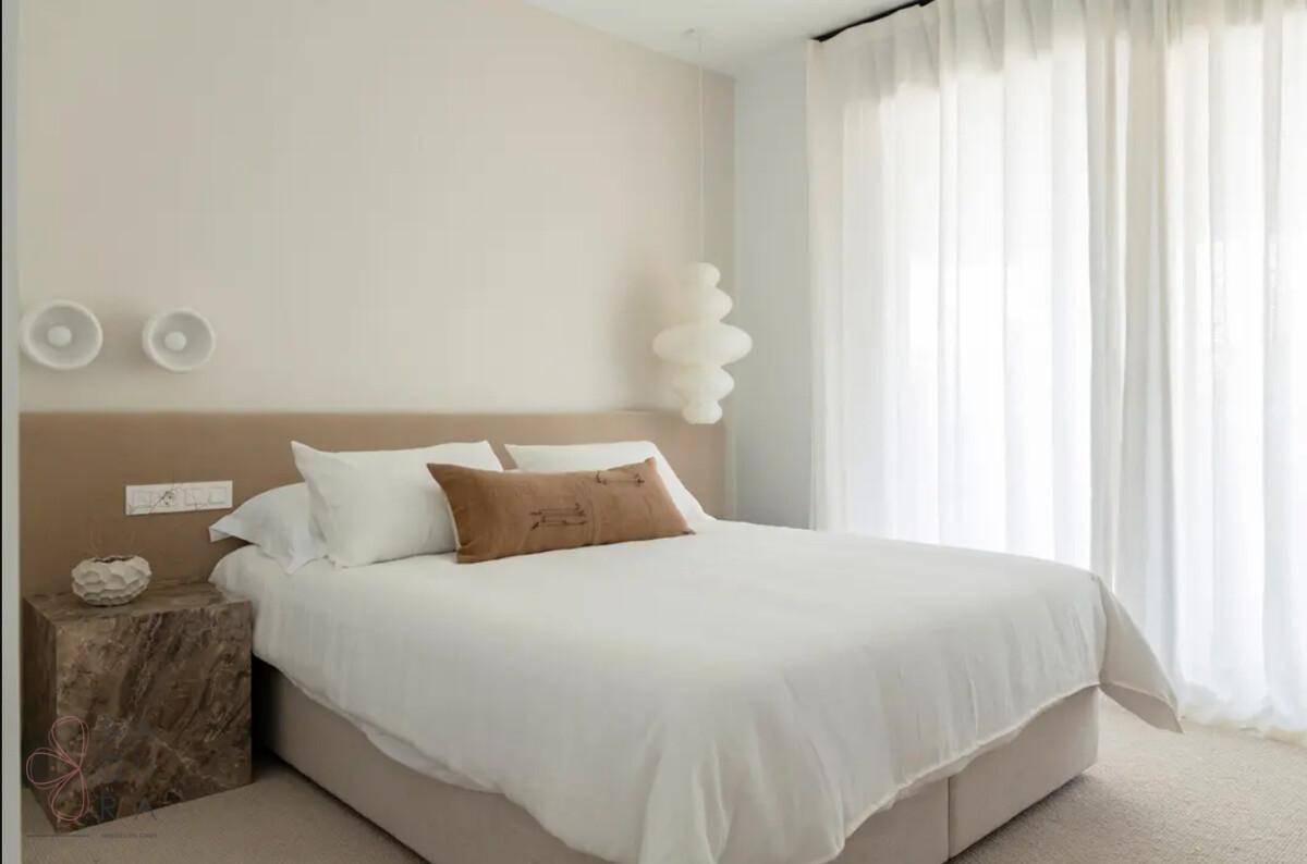 Helles Schlafzimmer mit Doppelbett, neutralen Farben und großen Fenstern für viel Tageslicht.