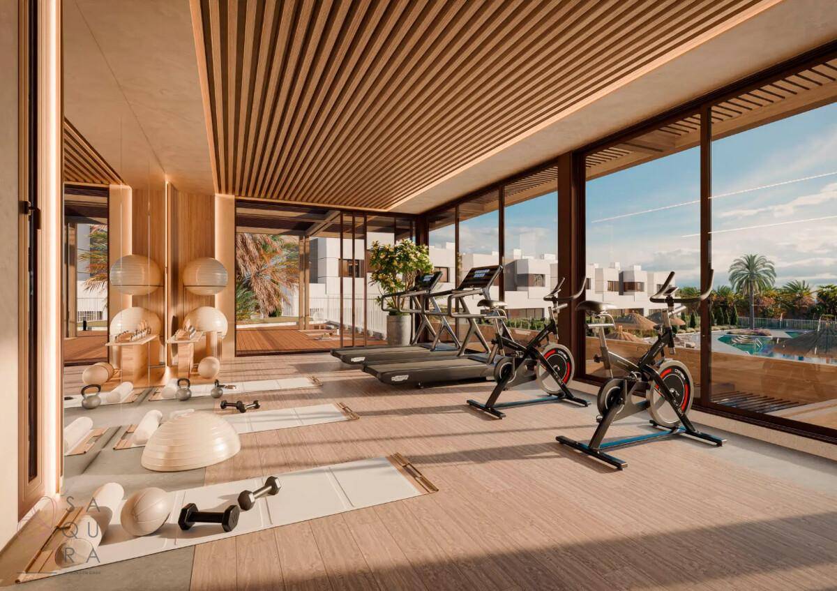 Moderner Fitnessraum mit Trainingsgeräten, großen Fenstern und Blick auf den Poolbereich.