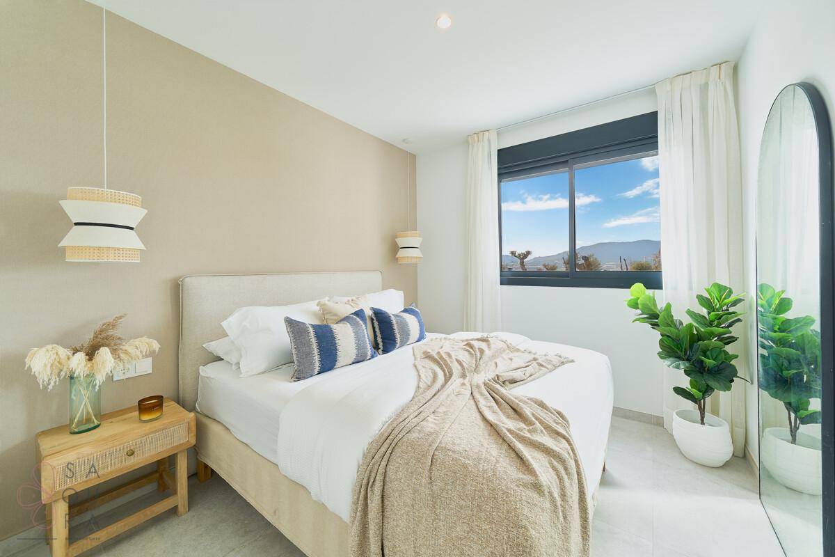 Modernes Schlafzimmer mit Doppelbett, beiger Wand und Fenster mit Blick ins Grüne.