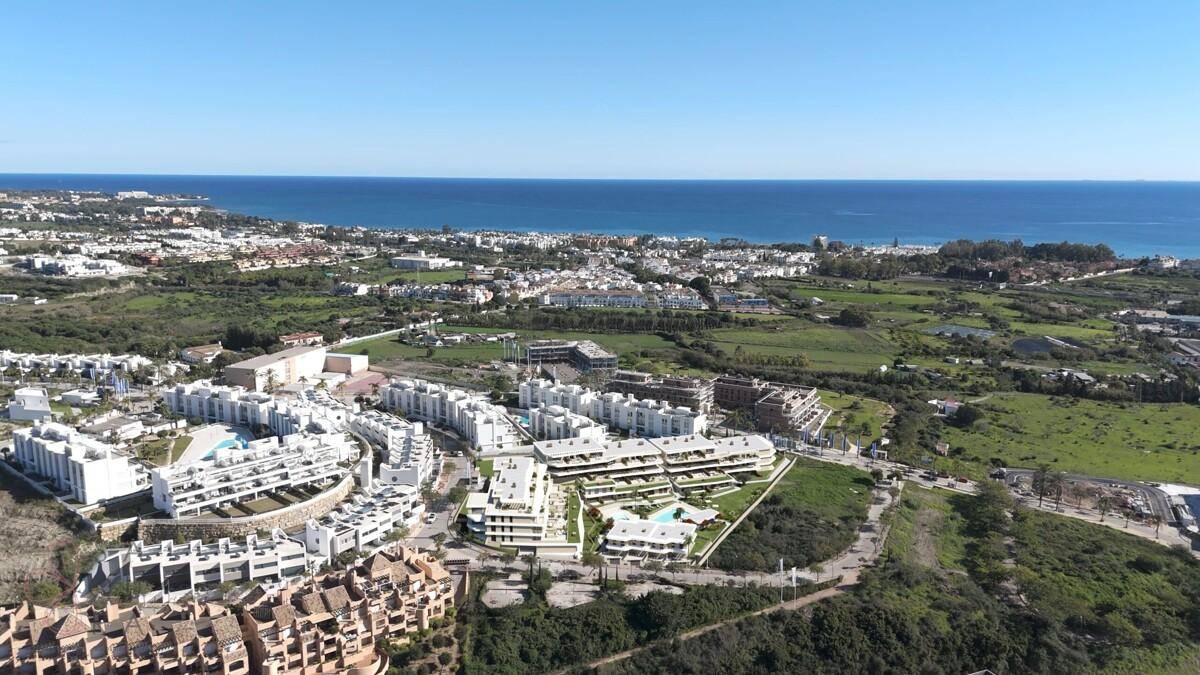 Weitläufiger Luftbildblick auf eine Küstenregion mit Wohnsiedlungen, viel Grün und dem strahlend blauen Meer.