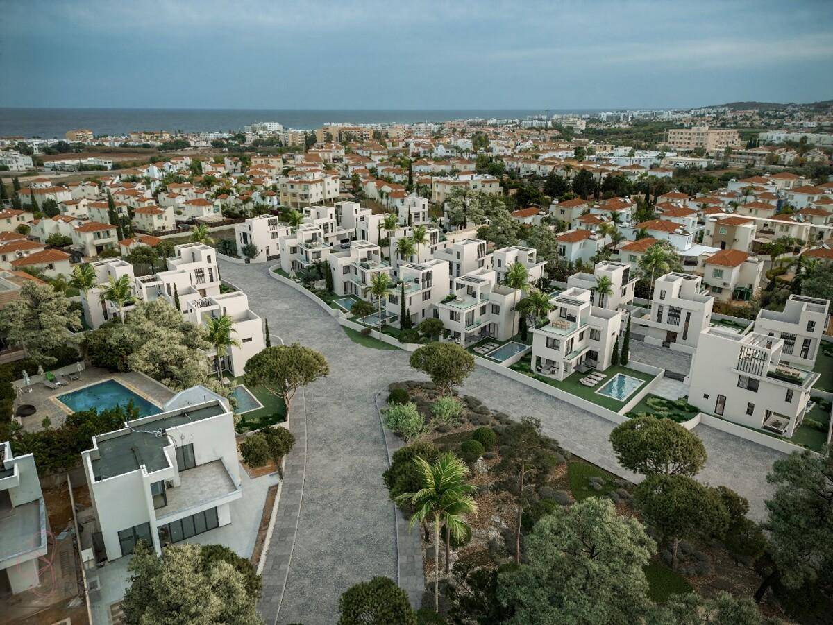 Luftaufnahme einer modernen Wohnsiedlung mit vielen Häusern, Pools und Meerblick in der Ferne.
