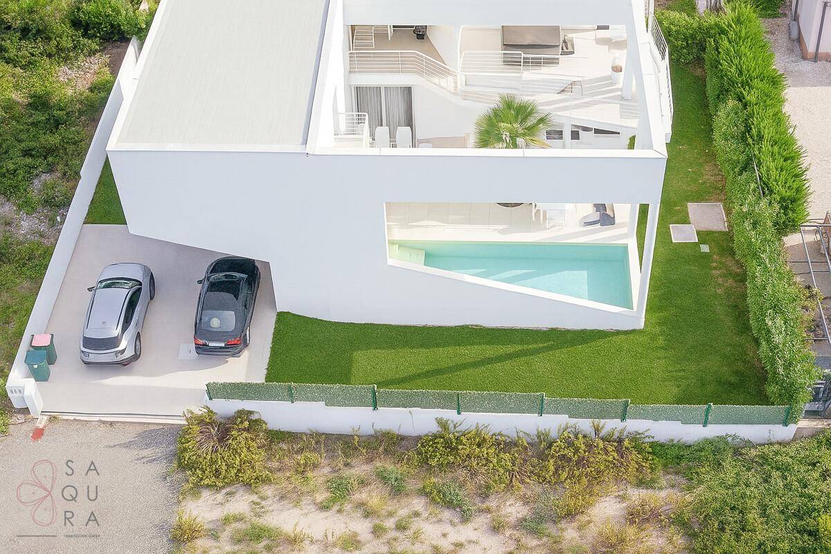 Seitenansicht der modernen Villa mit integriertem Pool, Parkplatz und gepflegtem Rasenbereich.