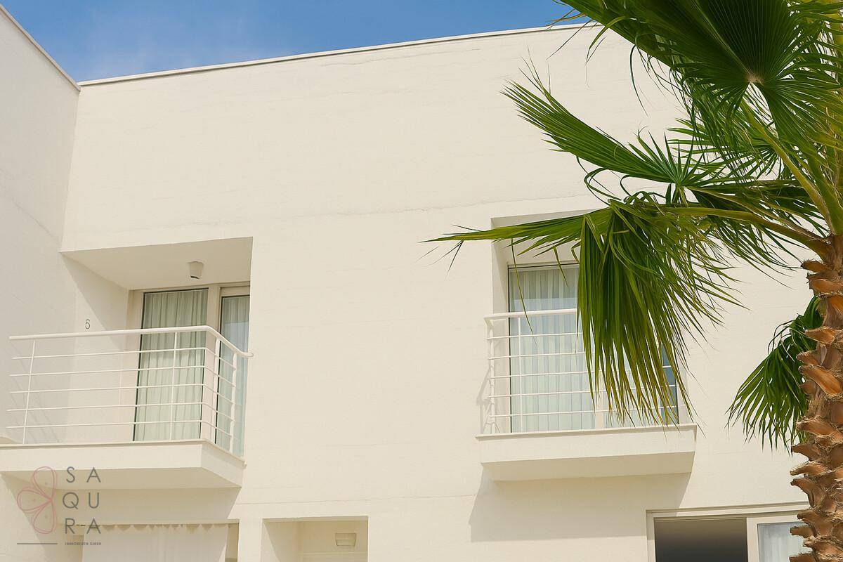 Weiße Fassade der modernen Villa mit zwei kleinen Balkonen und einer Palme im Vordergrund.