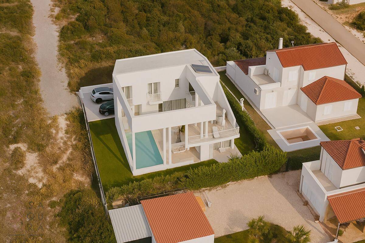 Moderne weiße Villa mit mehreren Balkonen, privatem Pool und umgebender Naturlandschaft.