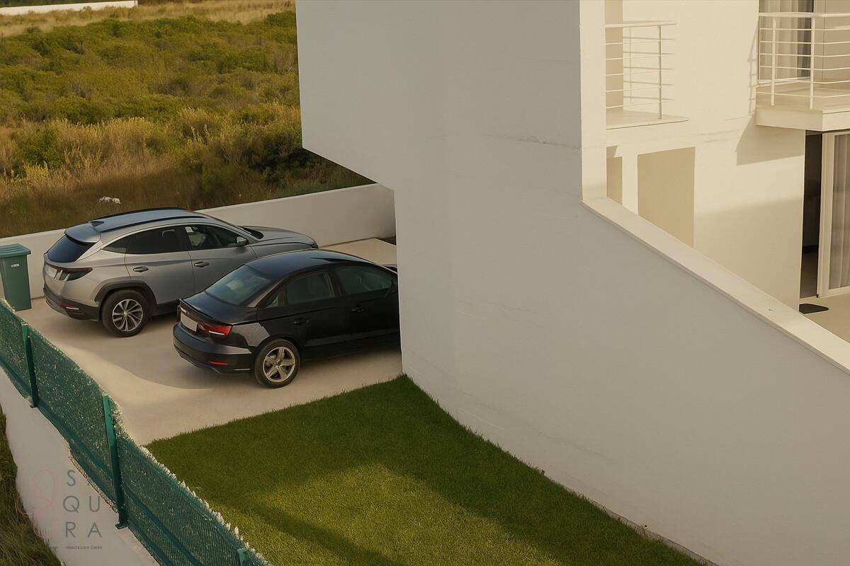 Parkplatzbereich der Villa mit zwei geparkten Autos und einem kleinen Rasenstück daneben.