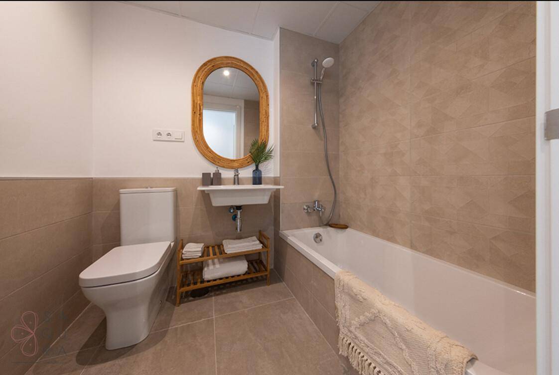 Modernes Badezimmer mit beigefarbenen Fliesen, Badewanne und wandmontierter Toilette.