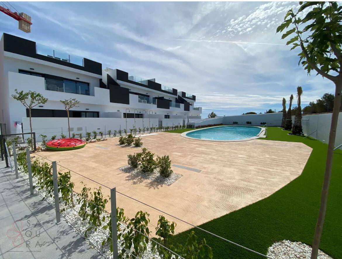 Außenbereich mit Pool, Kunstrasen und modernen Gebäuden unter blauem Himmel.