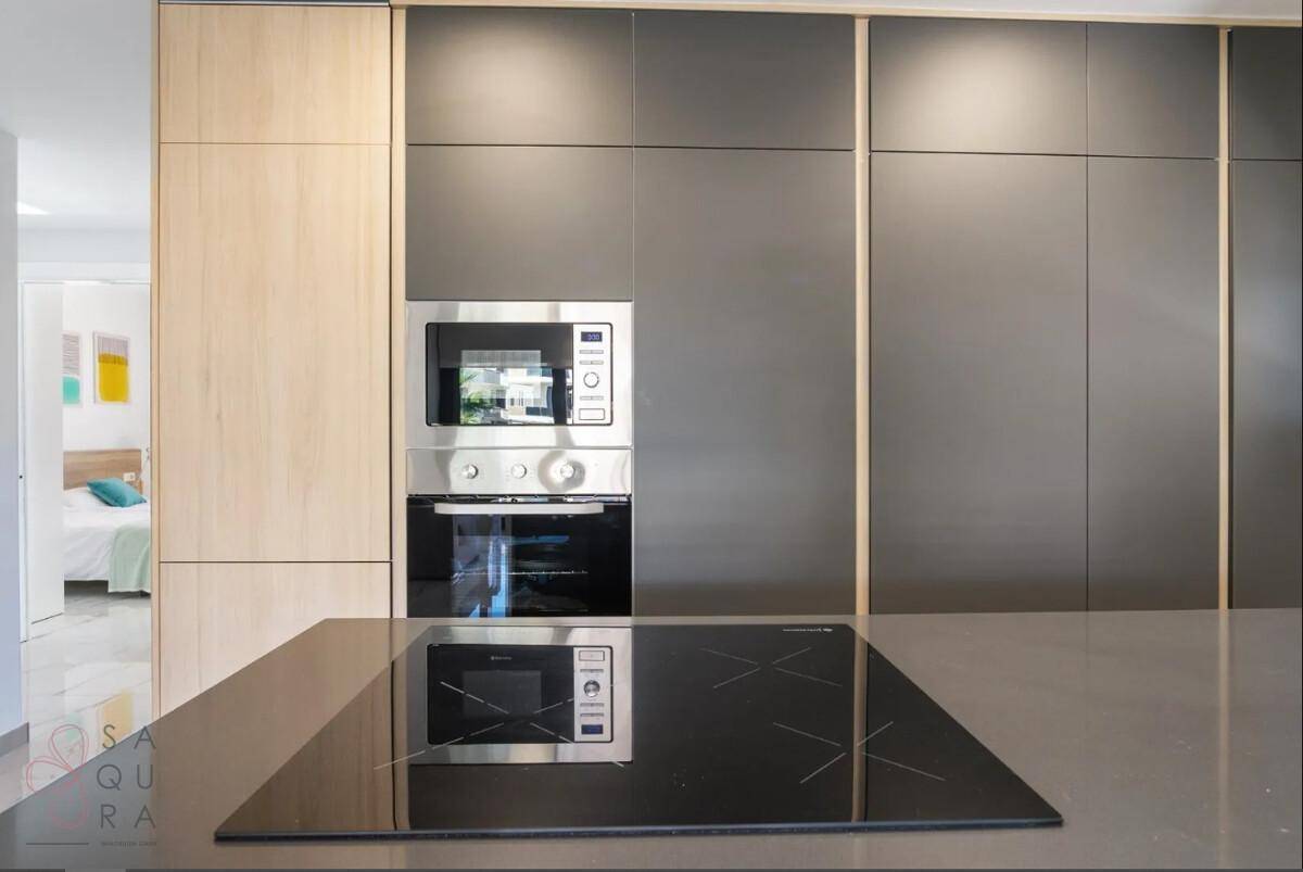 Moderne Einbauküche mit Induktionskochfeld, Backofen und Mikrowelle in dunklen und hellen Holztönen.