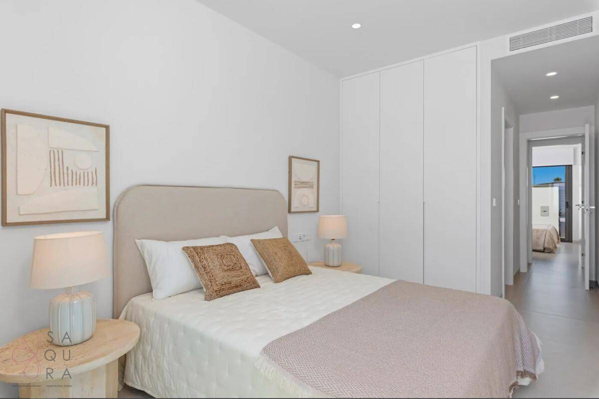 Helles Schlafzimmer mit Doppelbett, integriertem Kleiderschrank und Zugang zu einem weiteren Raum.