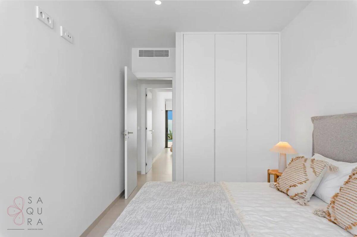 Schlafzimmer mit integriertem weißen Kleiderschrank und Blick in den Flur.