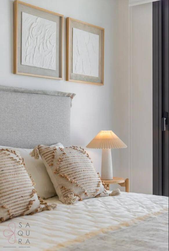 Gemütliches Schlafzimmer mit hellem Kopfteil, Nachttischlampe und minimalistischer Wandkunst.