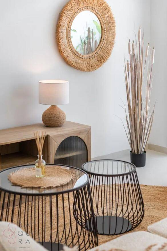 Stilvolle Dekoration im Wohnbereich mit Rattan-Spiegel, Tischlampe und modernen Beistelltischen.