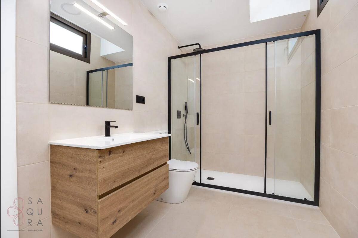Zeitgemäßes Badezimmer mit Duschkabine, Holzwaschtisch und Fenster für ausreichend Helligkeit.
