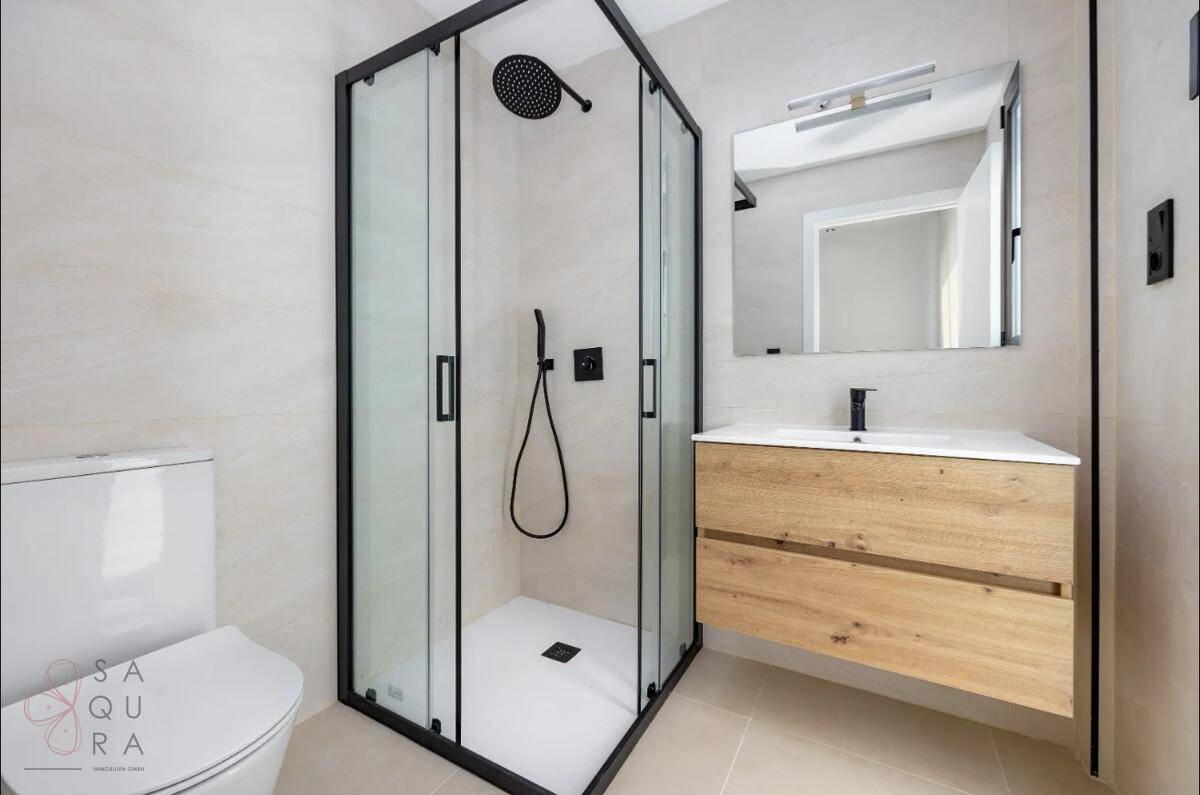 Modernes Badezimmer mit Duschkabine, Holzwaschtisch und Wand-WC in hellen Farbtönen.