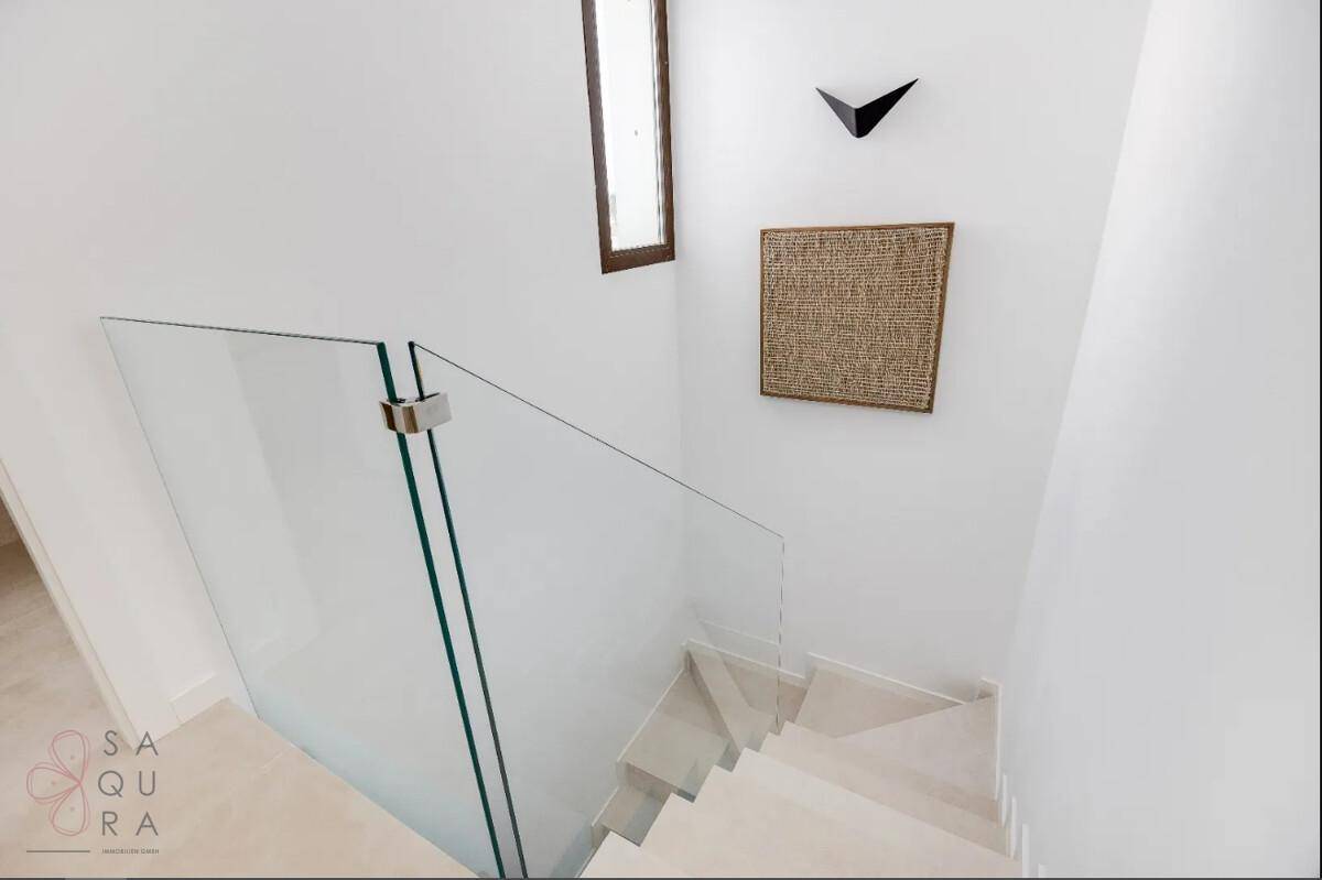Moderne Treppe mit Glasgeländer und hellen Stufen, die die verschiedenen Ebenen verbindet.
