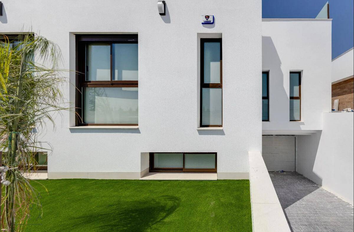 Moderne weiße Fassade mit verschiedenen Fenstergrößen und einem gepflegten Vorgarten.
