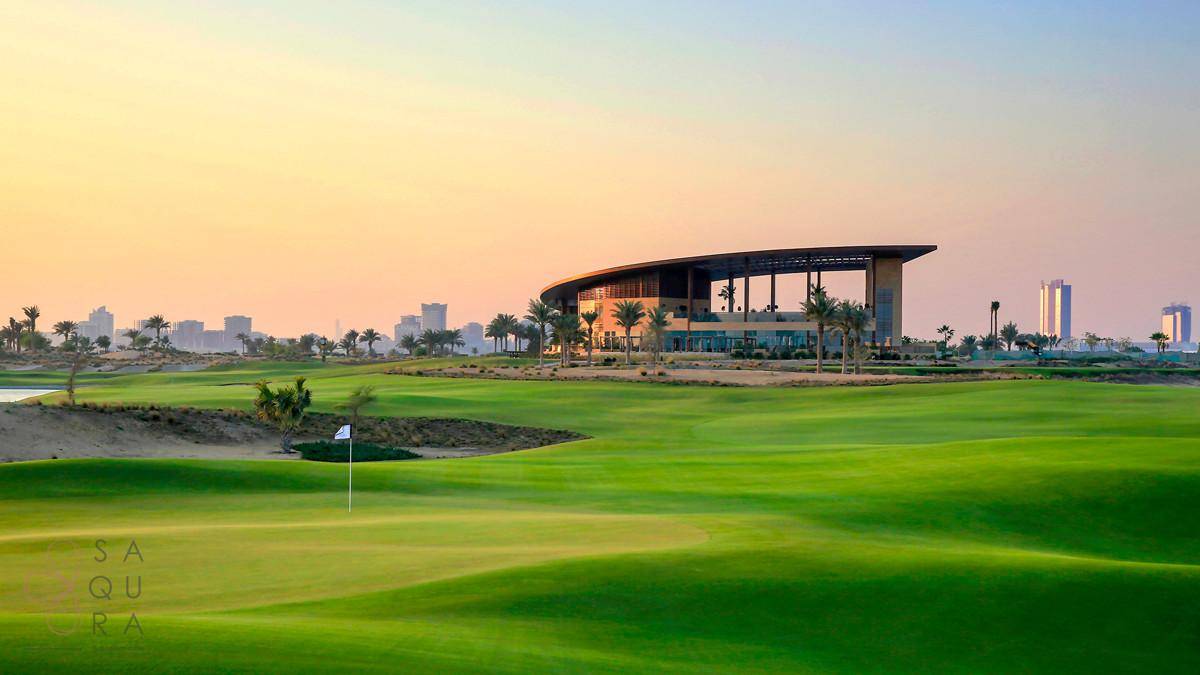 Weitläufiger Golfplatz mit modernem Clubhaus und Stadtpanorama bei Sonnenuntergang.