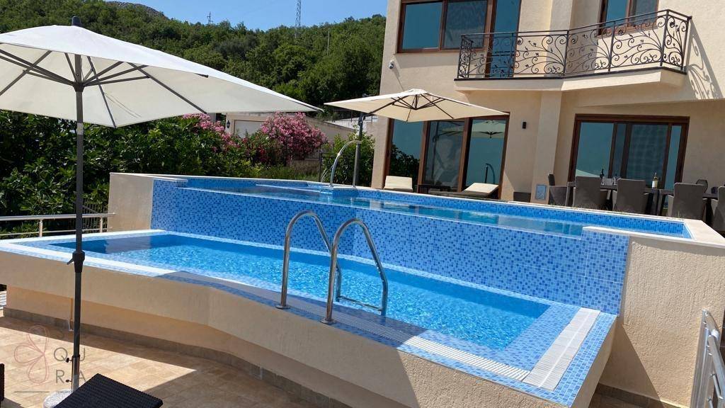 Außenbereich mit Pool, Sonnenliegen und einer möblierten Terrasse vor dem modernen Gebäude.