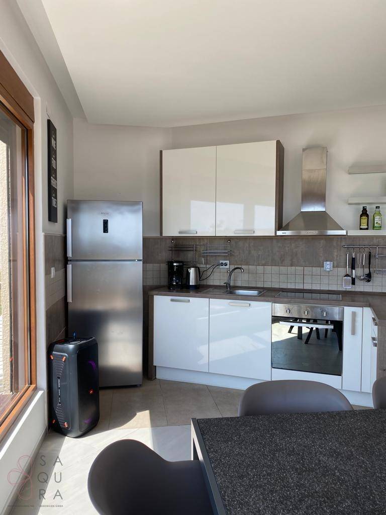Moderne Küche mit weißen Hochglanzschränken, Edelstahlgeräten und großem Fenster.