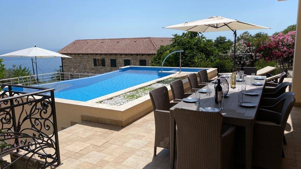 Große Terrasse mit Esstisch, Pool und Panoramablick auf das Meer und die grüne Umgebung.