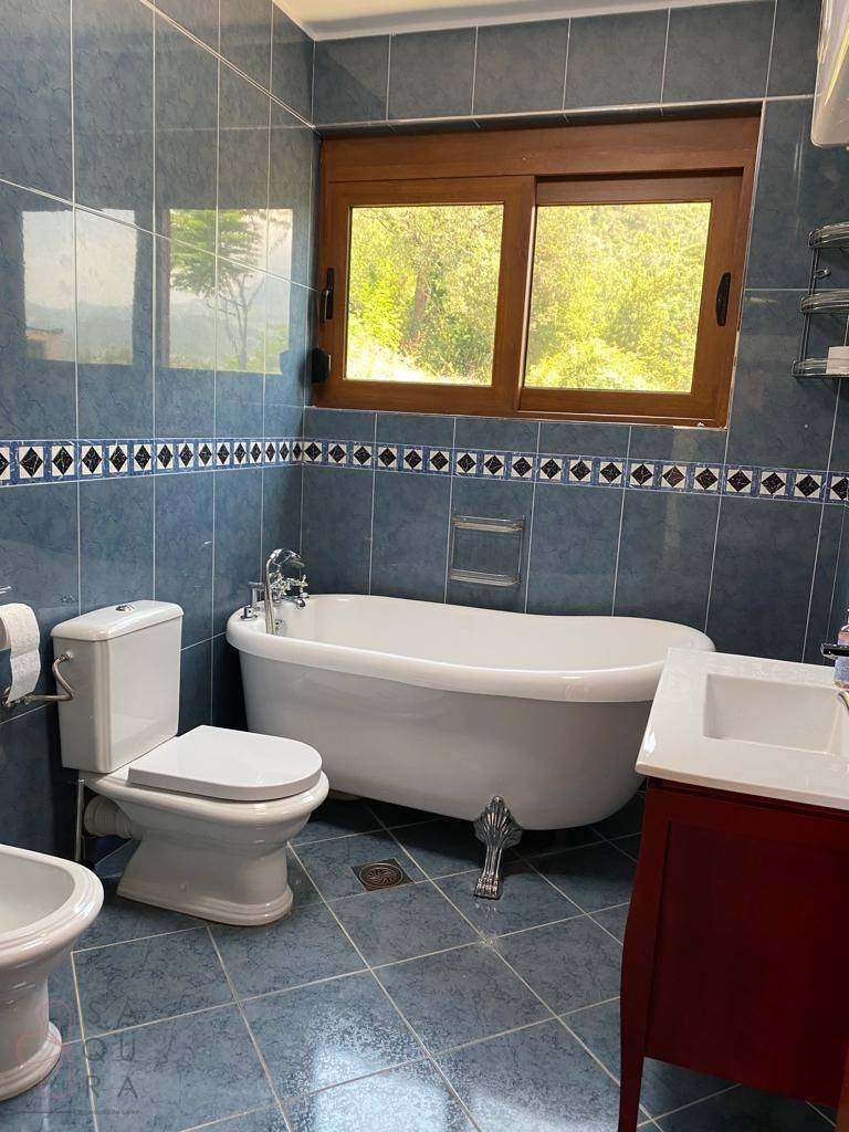 Badezimmer mit blauen Fliesen, freistehender Badewanne, WC und Fenster.