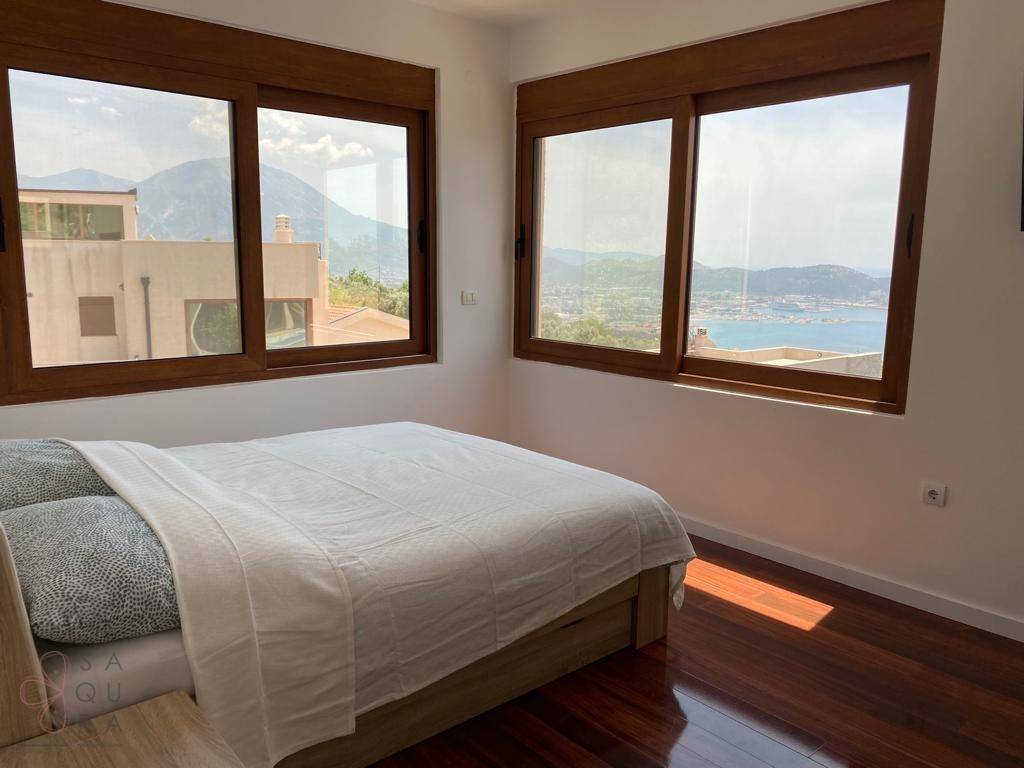 Schlafzimmer mit Holzboden und weitem Blick auf das Meer und die Berge durch große Fenster.