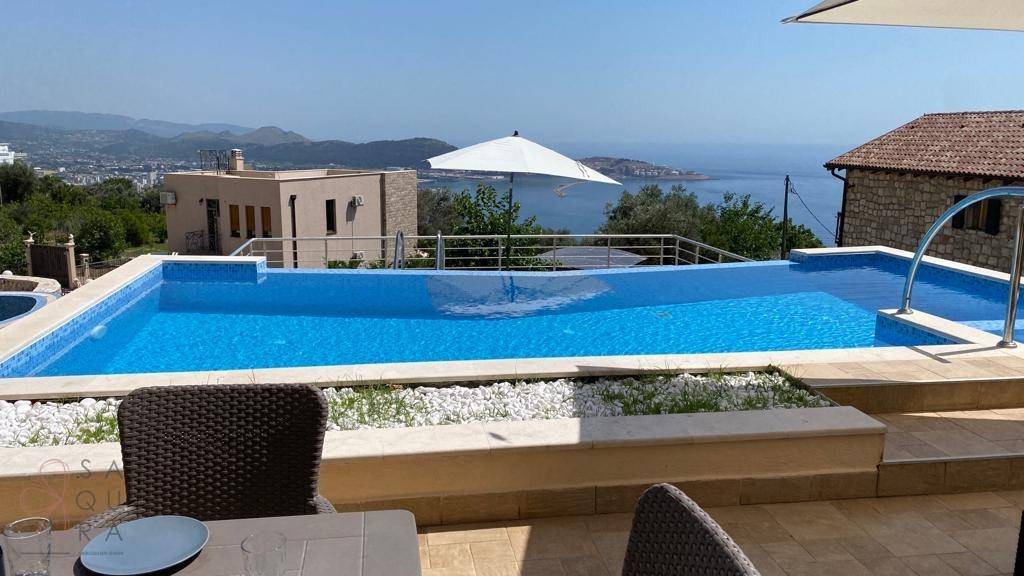 Poolbereich mit blauen Fliesen und weitem Blick auf das glitzernde Meer und die Küste.