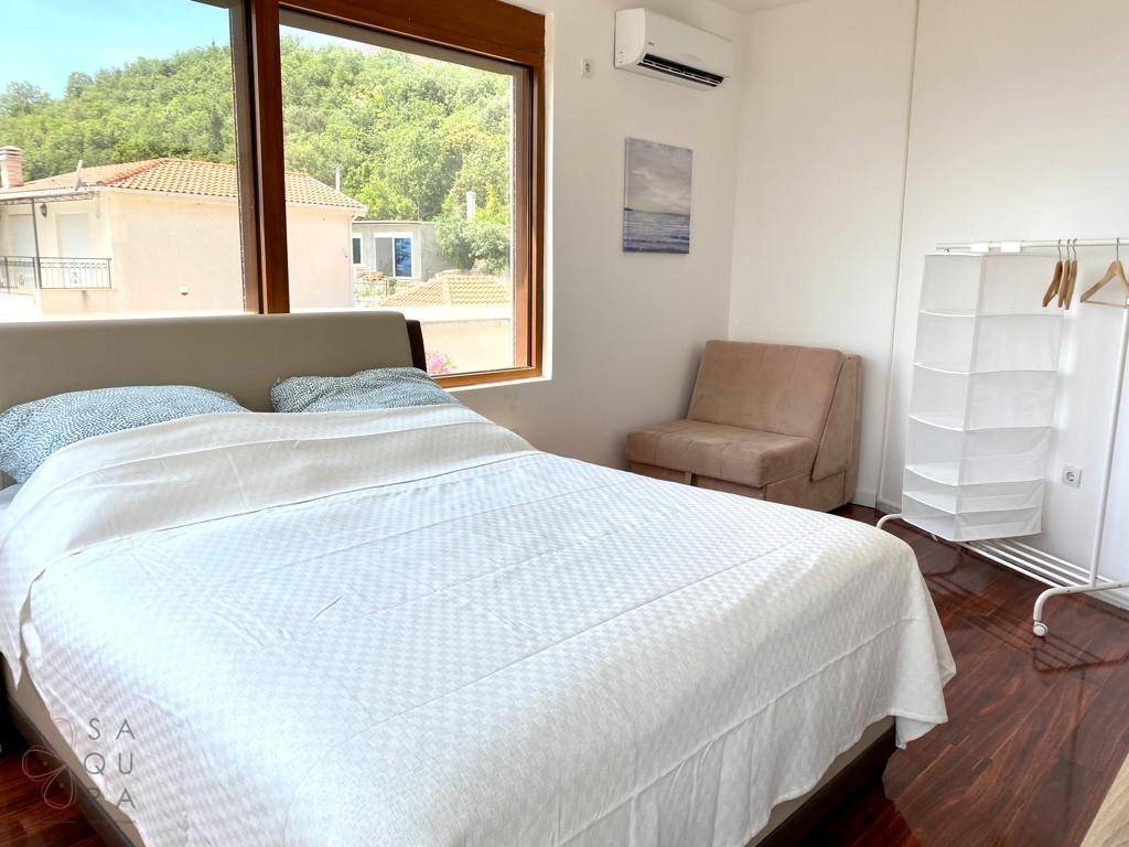 Helles Schlafzimmer mit Holzboden, Klimaanlage und großem Fenster mit Blick ins Grüne.
